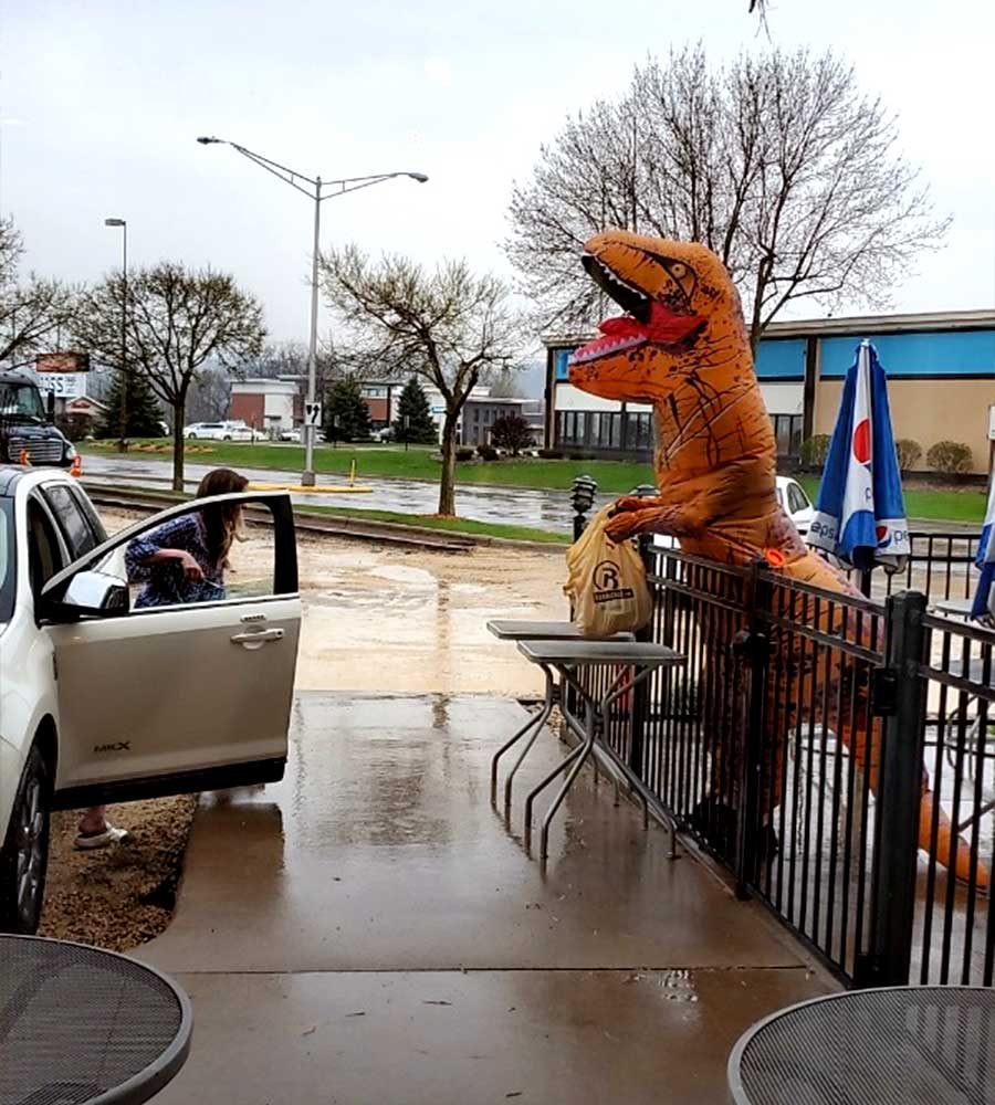 a dinosaur costume holding a bag for a customer picking it up from their car