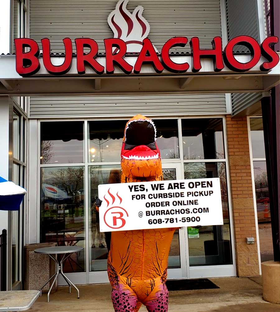 a dinosaur costume holding a sign in front of a Burrachos location